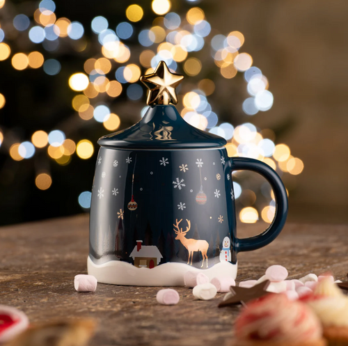 Decorative mug with reindeer design on a wooden surface with blurred lights in the background
