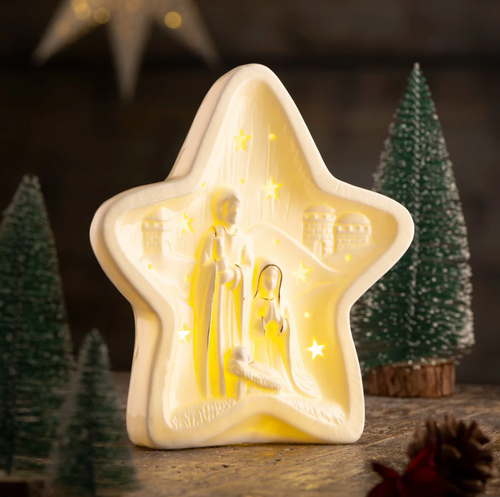 Star-shaped nativity scene light with a dark background and Christmas trees.